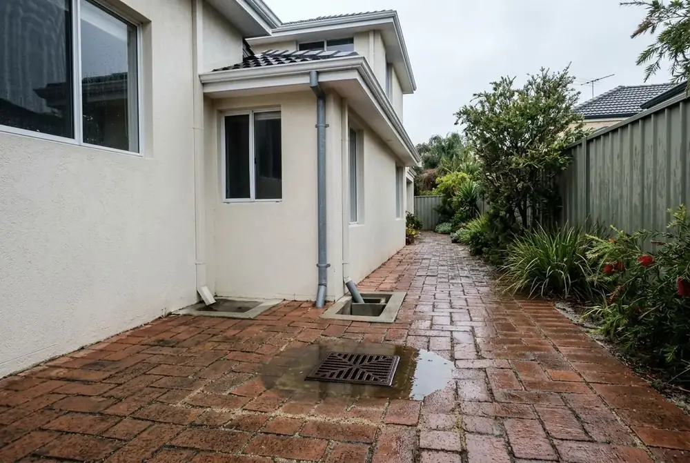 Illustration of water pooling over a soakwell grate in Perth paving after rain, with the surrounding pavers starting to sink